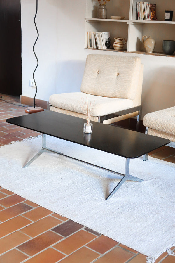 Table basse design années 70 avec plateau noir rectangulaire et piétement en acier brossé en forme de patins.