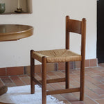 Lot de quatre chaises vintage des années 60 en chêne massif avec assise en paille tressée, style Charlotte Perriand, posées sur un sol en carrelage rouge.