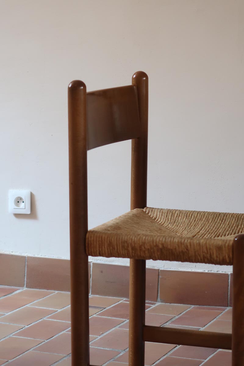 Lot de quatre chaises vintage des années 60 en chêne massif avec assise en paille tressée, style Charlotte Perriand, posées sur un sol en carrelage rouge.