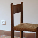 Lot de quatre chaises vintage des années 60 en chêne massif avec assise en paille tressée, style Charlotte Perriand, posées sur un sol en carrelage rouge.