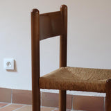 Lot de quatre chaises vintage des années 60 en chêne massif avec assise en paille tressée, style Charlotte Perriand, posées sur un sol en carrelage rouge.