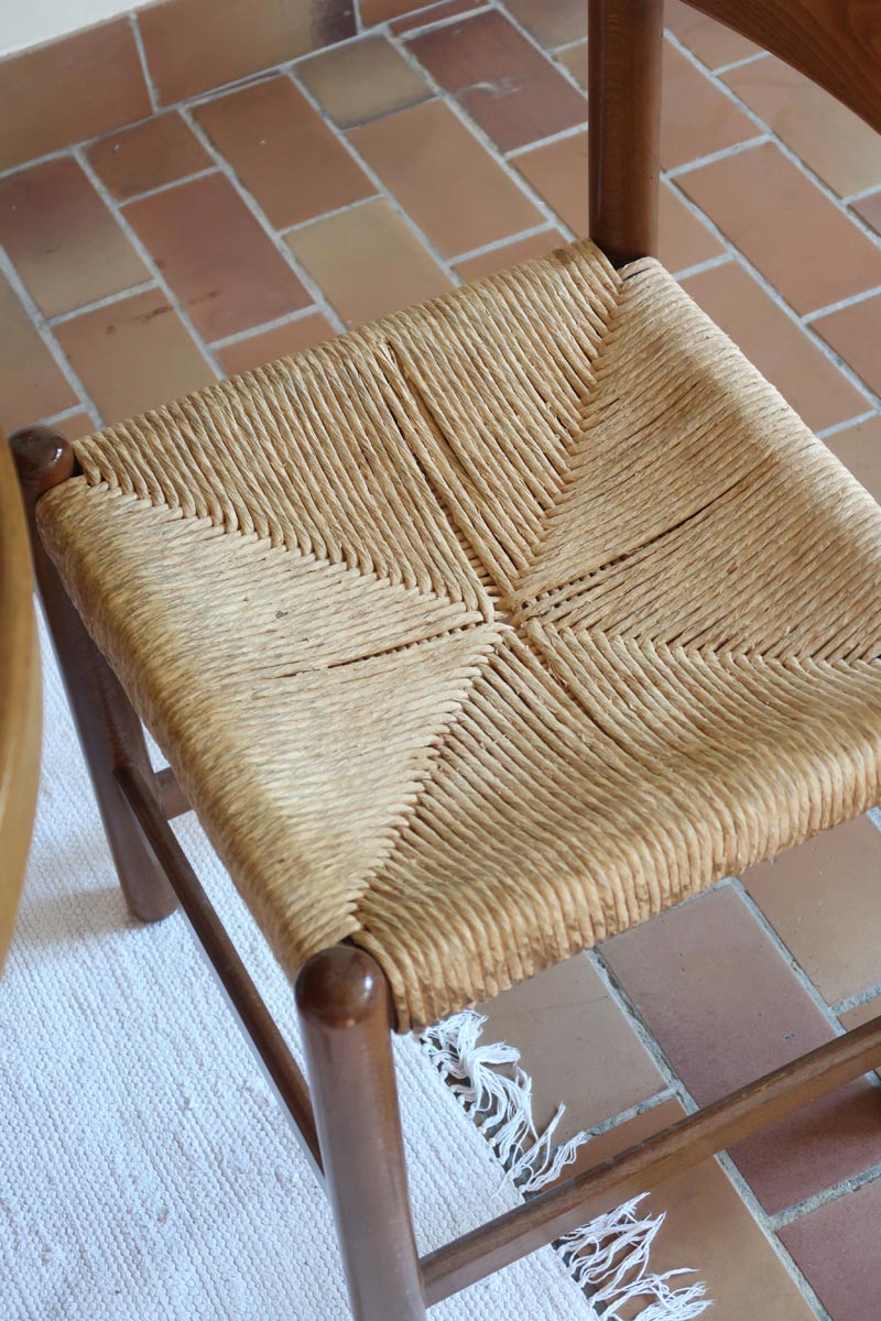 Lot de quatre chaises vintage des années 60 en chêne massif avec assise en paille tressée, style Charlotte Perriand, posées sur un sol en carrelage rouge.