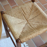 Lot de quatre chaises vintage des années 60 en chêne massif avec assise en paille tressée, style Charlotte Perriand, posées sur un sol en carrelage rouge.