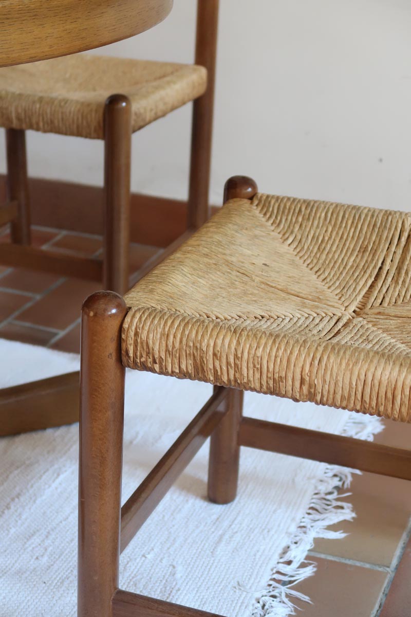 Lot de quatre chaises vintage des années 60 en chêne massif avec assise en paille tressée, style Charlotte Perriand, posées sur un sol en carrelage rouge.