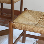 Lot de quatre chaises vintage des années 60 en chêne massif avec assise en paille tressée, style Charlotte Perriand, posées sur un sol en carrelage rouge.