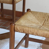 Lot de quatre chaises vintage des années 60 en chêne massif avec assise en paille tressée, style Charlotte Perriand, posées sur un sol en carrelage rouge.