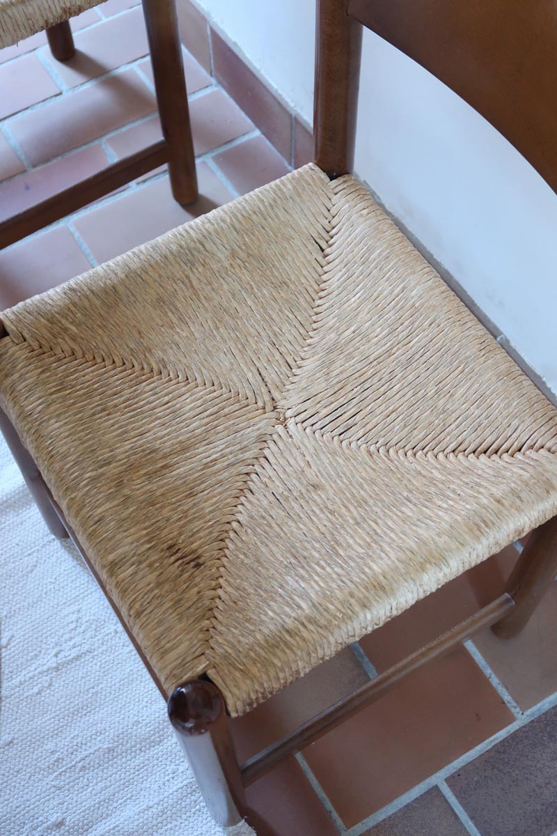 Lot de quatre chaises vintage des années 60 en chêne massif avec assise en paille tressée, style Charlotte Perriand, posées sur un sol en carrelage rouge.