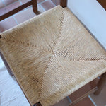 Lot de quatre chaises vintage des années 60 en chêne massif avec assise en paille tressée, style Charlotte Perriand, posées sur un sol en carrelage rouge.