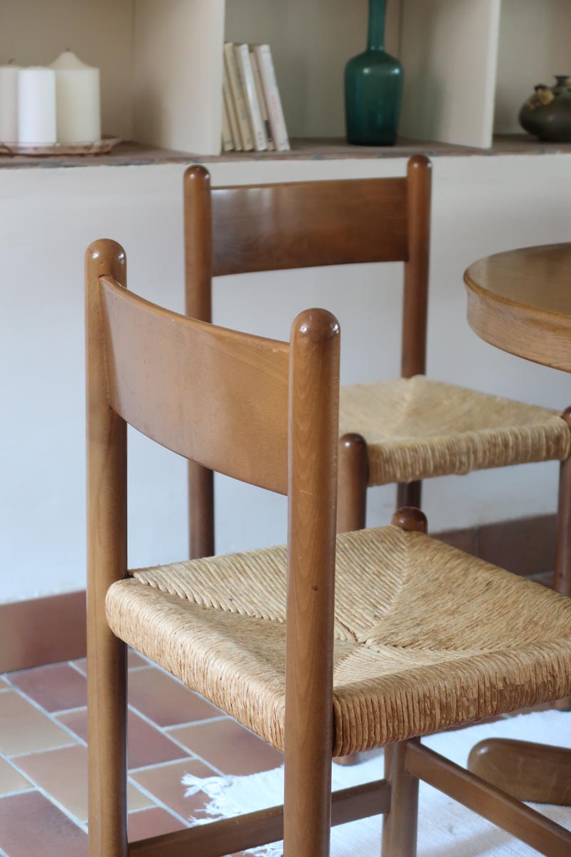 Lot de quatre chaises vintage des années 60 en chêne massif avec assise en paille tressée, style Charlotte Perriand, posées sur un sol en carrelage rouge.