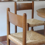 Lot de quatre chaises vintage des années 60 en chêne massif avec assise en paille tressée, style Charlotte Perriand, posées sur un sol en carrelage rouge.