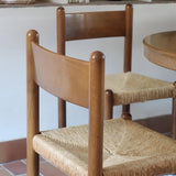 Lot de quatre chaises vintage des années 60 en chêne massif avec assise en paille tressée, style Charlotte Perriand, posées sur un sol en carrelage rouge.