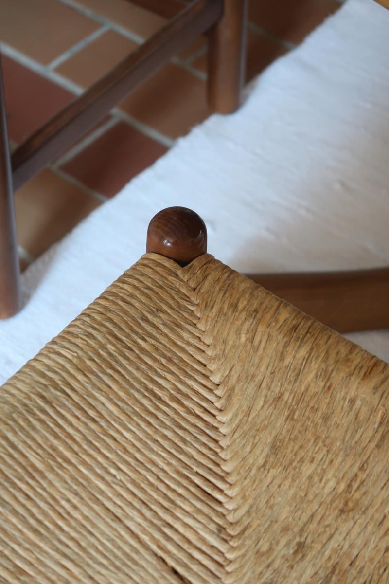 Lot de quatre chaises vintage des années 60 en chêne massif avec assise en paille tressée, style Charlotte Perriand, posées sur un sol en carrelage rouge.