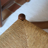 Lot de quatre chaises vintage des années 60 en chêne massif avec assise en paille tressée, style Charlotte Perriand, posées sur un sol en carrelage rouge.