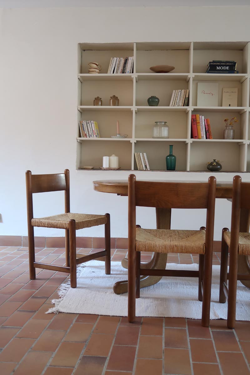 Lot de quatre chaises vintage des années 60 en chêne massif avec assise en paille tressée, style Charlotte Perriand, posées sur un sol en carrelage rouge.