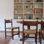 Lot de quatre chaises vintage des années 60 en chêne massif avec assise en paille tressée, style Charlotte Perriand, posées sur un sol en carrelage rouge.