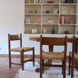 Lot de quatre chaises vintage des années 60 en chêne massif avec assise en paille tressée, style Charlotte Perriand, posées sur un sol en carrelage rouge.