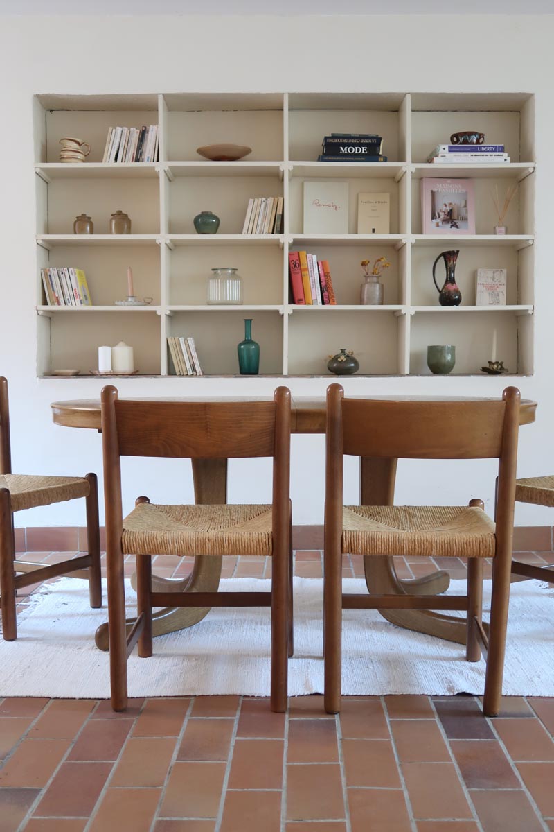 Lot de quatre chaises vintage des années 60 en chêne massif avec assise en paille tressée, style Charlotte Perriand, posées sur un sol en carrelage rouge.
