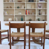 Lot de quatre chaises vintage des années 60 en chêne massif avec assise en paille tressée, style Charlotte Perriand, posées sur un sol en carrelage rouge.