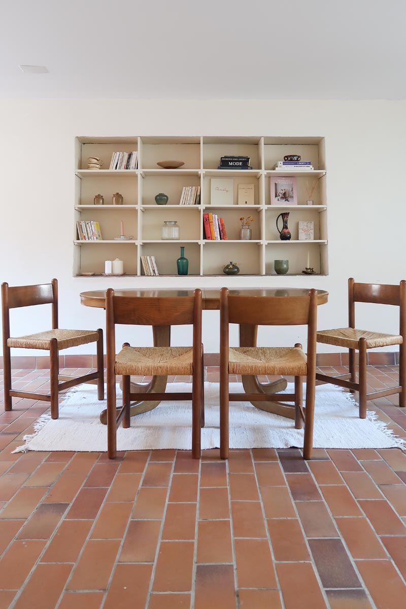 Lot de quatre chaises vintage des années 60 en chêne massif avec assise en paille tressée, style Charlotte Perriand, posées sur un sol en carrelage rouge.