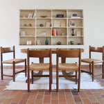 Lot de quatre chaises vintage des années 60 en chêne massif avec assise en paille tressée, style Charlotte Perriand, posées sur un sol en carrelage rouge.