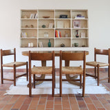 Lot de quatre chaises vintage des années 60 en chêne massif avec assise en paille tressée, style Charlotte Perriand, posées sur un sol en carrelage rouge.