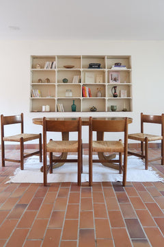 Lot de quatre chaises vintage des années 60 en chêne massif avec assise en paille tressée, style Charlotte Perriand, posées sur un sol en carrelage rouge.