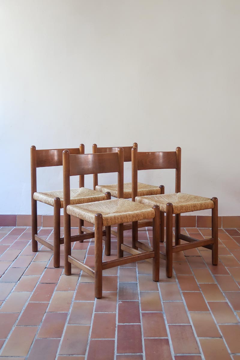 Lot de quatre chaises vintage des années 60 en chêne massif avec assise en paille tressée, style Charlotte Perriand, posées sur un sol en carrelage rouge.