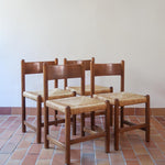 Lot de quatre chaises vintage des années 60 en chêne massif avec assise en paille tressée, style Charlotte Perriand, posées sur un sol en carrelage rouge.