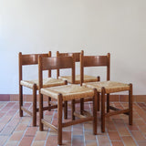Lot de quatre chaises vintage des années 60 en chêne massif avec assise en paille tressée, style Charlotte Perriand, posées sur un sol en carrelage rouge.
