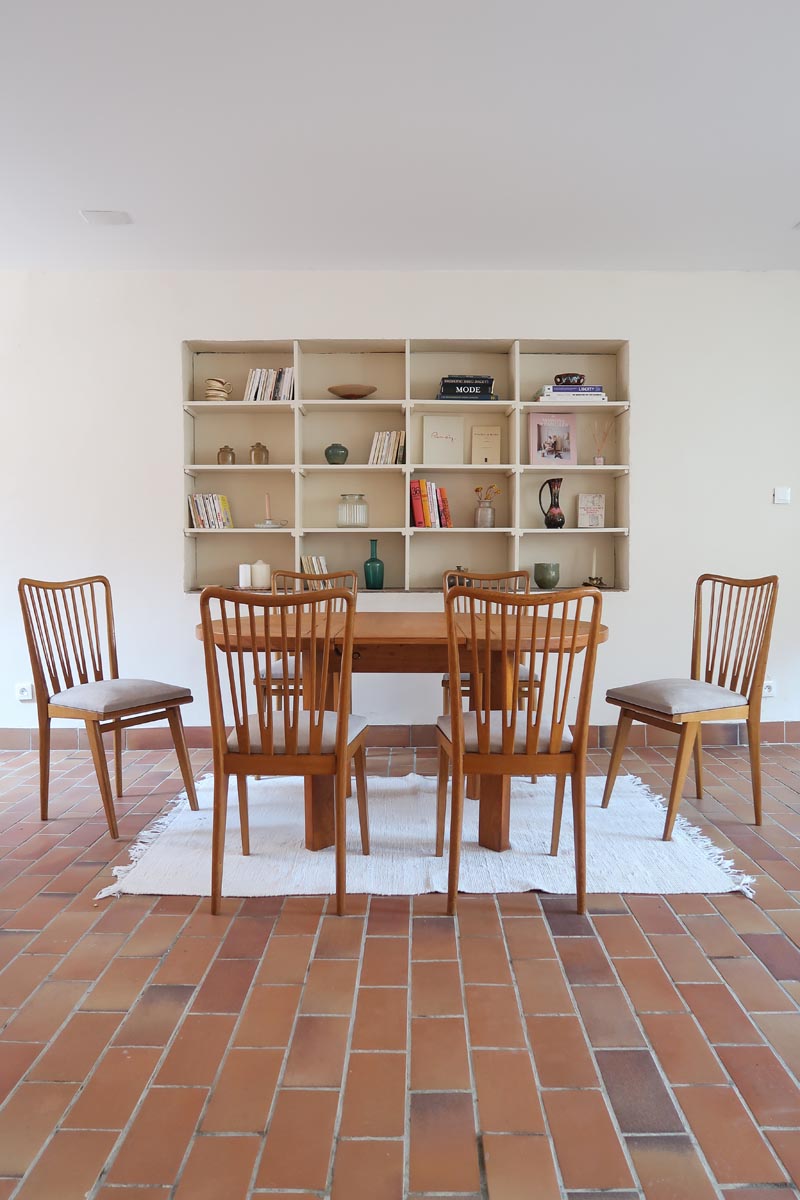 Lot de six chaises vintage scandinaves des années 60 en hêtre massif, dossier à barreaux galbés et assise en tissu clair, posées sur carrelage rouge.