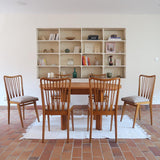 Lot de six chaises vintage scandinaves des années 60 en hêtre massif, dossier à barreaux galbés et assise en tissu clair, posées sur carrelage rouge.