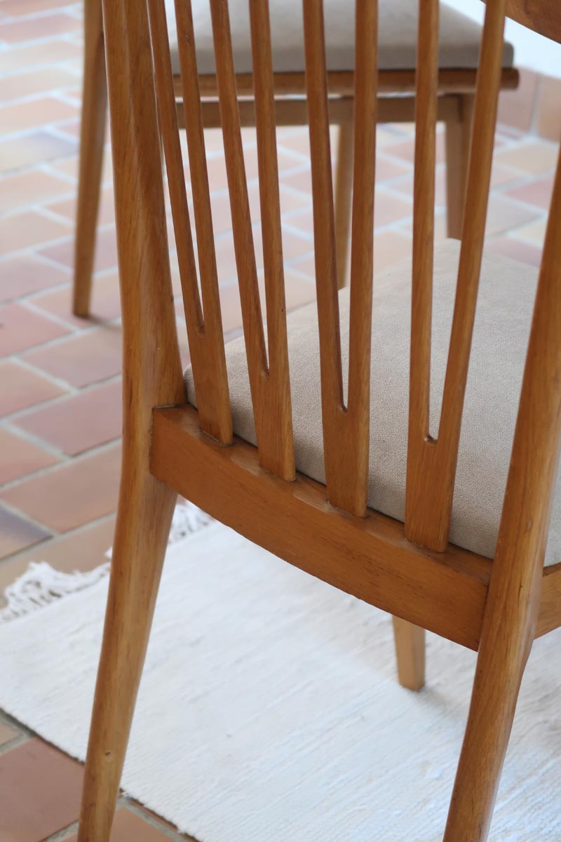 Lot de six chaises vintage scandinaves des années 60 en hêtre massif, dossier à barreaux galbés et assise en tissu clair, posées sur carrelage rouge.