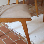 Lot de six chaises vintage scandinaves des années 60 en hêtre massif, dossier à barreaux galbés et assise en tissu clair, posées sur carrelage rouge.