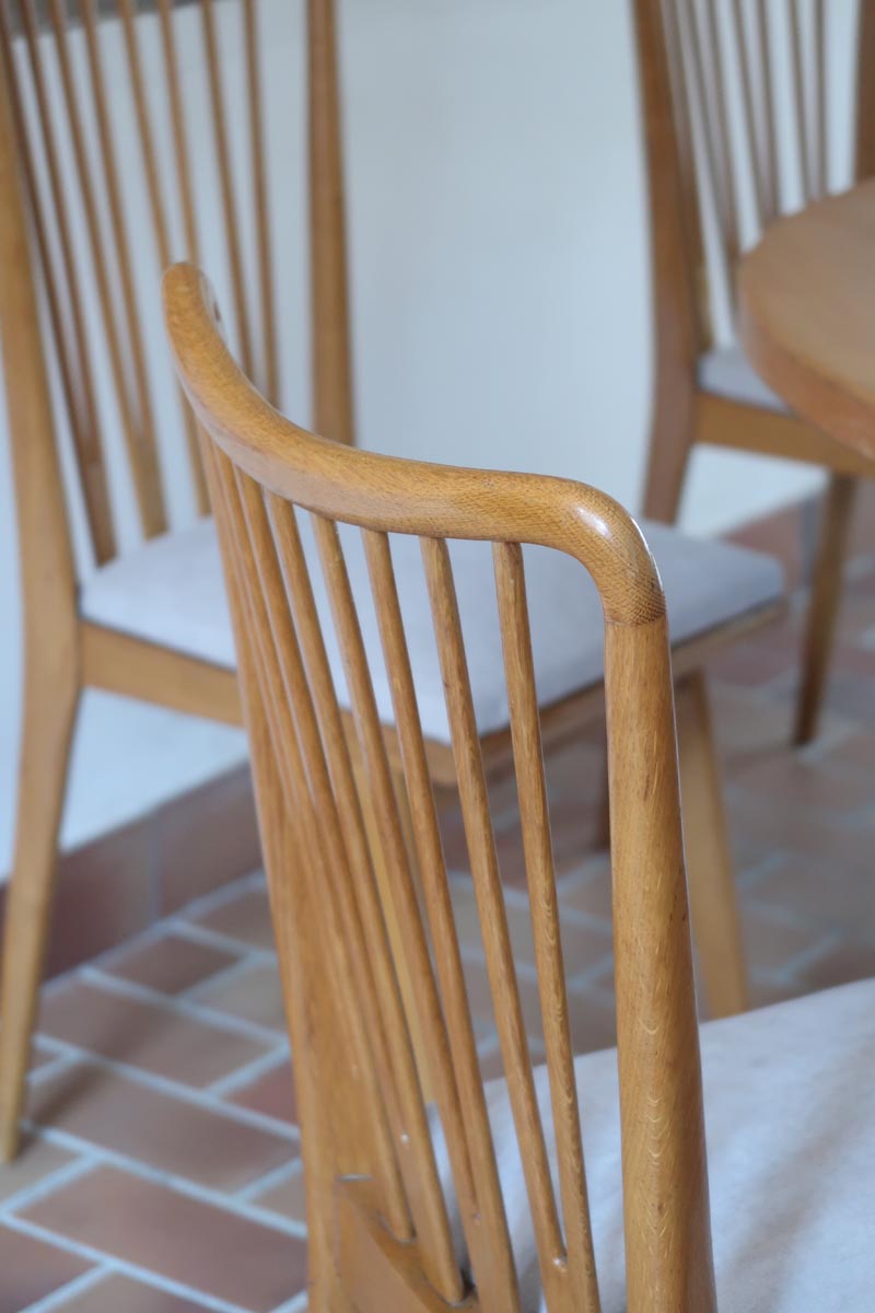 Lot de six chaises vintage scandinaves des années 60 en hêtre massif, dossier à barreaux galbés et assise en tissu clair, posées sur carrelage rouge.