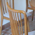 Lot de six chaises vintage scandinaves des années 60 en hêtre massif, dossier à barreaux galbés et assise en tissu clair, posées sur carrelage rouge.