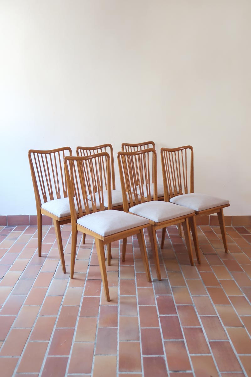 Lot de six chaises vintage scandinaves des années 60 en hêtre massif, dossier à barreaux galbés et assise en tissu clair, posées sur carrelage rouge.