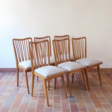 Lot de six chaises vintage scandinaves des années 60 en hêtre massif, dossier à barreaux galbés et assise en tissu clair, posées sur carrelage rouge.