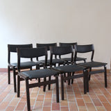Suite de 6 chaises danoises vintage années 60, bois teinté brun, pieds arrière cintrés filant jusqu'au dossier bandeau, assises et dossiers retapissés en skaï noir