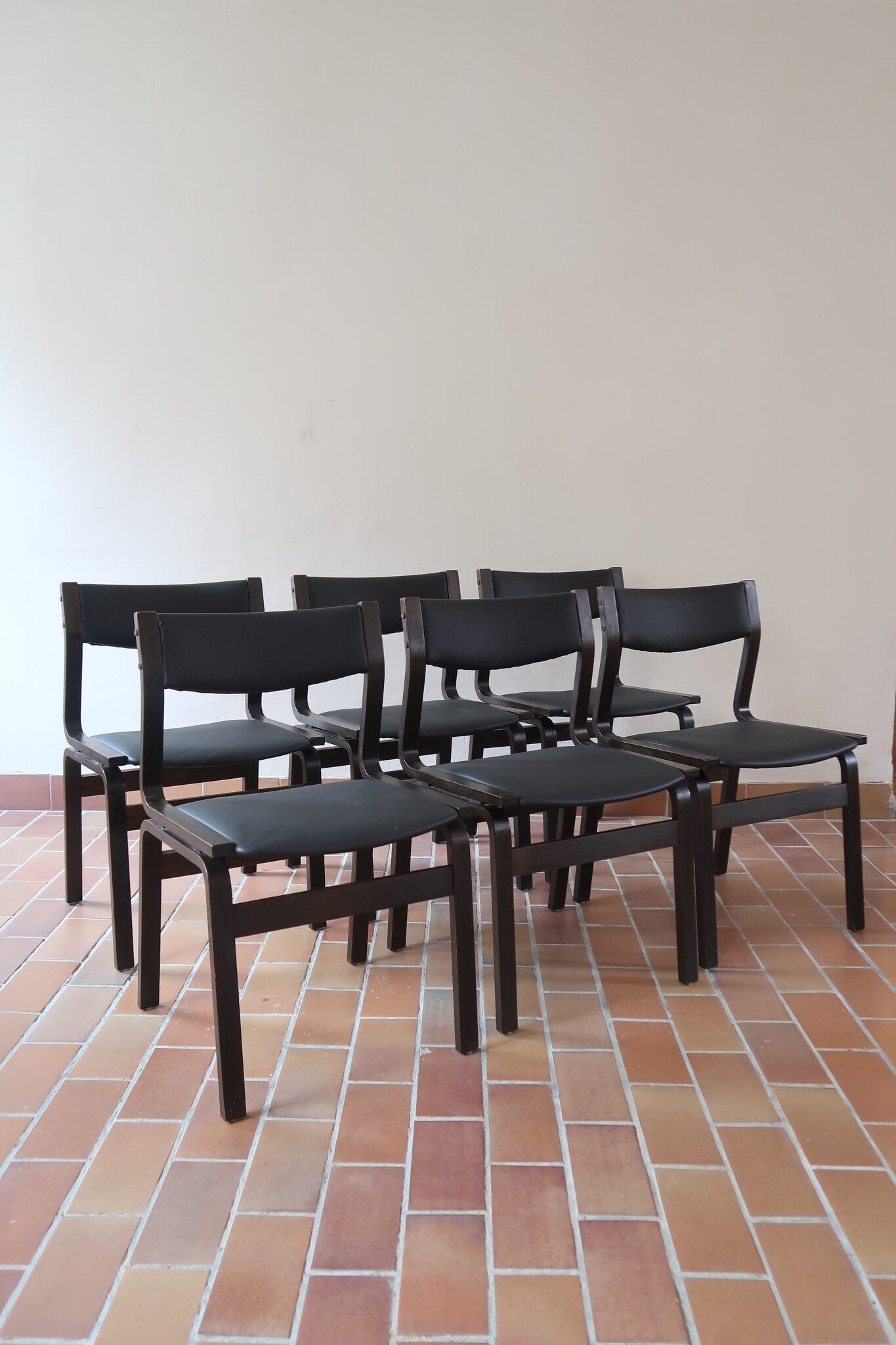 Suite de 6 chaises danoises vintage années 60, bois teinté brun, pieds arrière cintrés filant jusqu'au dossier bandeau, assises et dossiers retapissés en skaï noir