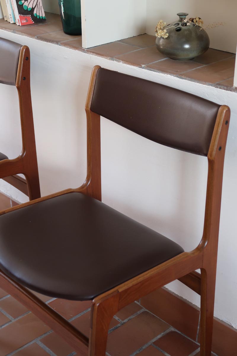 Lot de cinq chaises scandinaves vintage en teck des années 60, style Erik Buch, avec assise et dossier en skaï marron, accompagné d’une sixième chaise offerte présentant une petite déchirure sur le dossier, présentées seules et en mise en situation.