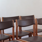 Lot de cinq chaises scandinaves vintage en teck des années 60, style Erik Buch, avec assise et dossier en skaï marron, accompagné d’une sixième chaise offerte présentant une petite déchirure sur le dossier, présentées seules et en mise en situation.