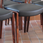 Lot de six chaises scandinaves vintage en teck massif avec assise et dossier en skaï noir, style Niels Otto Møller ou Erik Buch, présentées seules et en mise en situation dans différents espaces.