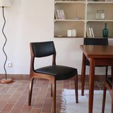 Lot de six chaises scandinaves vintage en teck massif avec assise et dossier en skaï noir, style Niels Otto Møller ou Erik Buch, présentées seules et en mise en situation dans différents espaces.