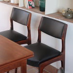 Lot de six chaises scandinaves vintage en teck massif avec assise et dossier en skaï noir, style Niels Otto Møller ou Erik Buch, présentées seules et en mise en situation dans différents espaces.