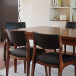 Lot de six chaises scandinaves vintage en teck massif avec assise et dossier en skaï noir, style Niels Otto Møller ou Erik Buch, présentées seules et en mise en situation dans différents espaces.