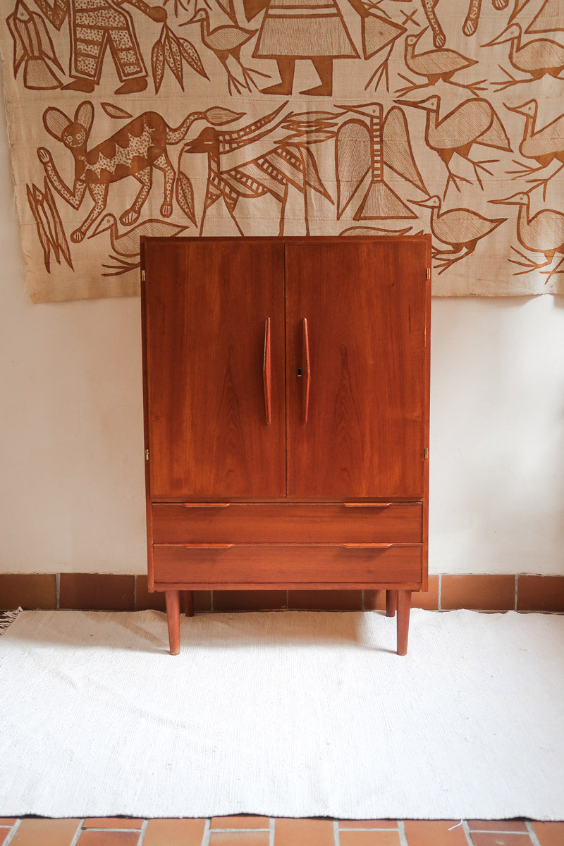 Armoire vintage en bois des années 60 avec deux portes, deux tiroirs, poignées sculptées et pieds compas.