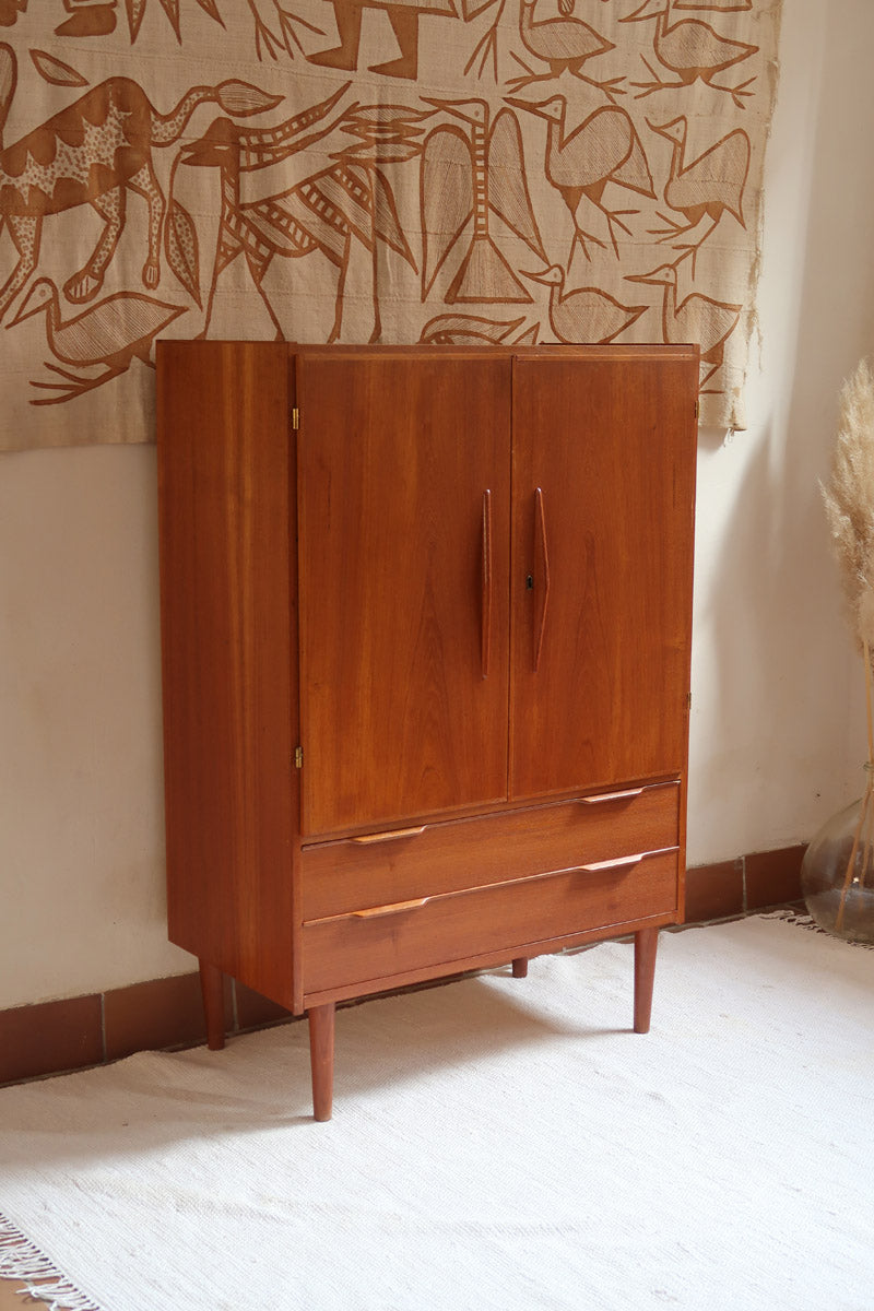 Armoire vintage en bois des années 60 avec deux portes, deux tiroirs, poignées sculptées et pieds compas.