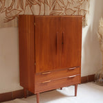 Armoire vintage en bois des années 60 avec deux portes, deux tiroirs, poignées sculptées et pieds compas.