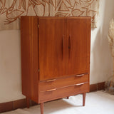 Armoire vintage en bois des années 60 avec deux portes, deux tiroirs, poignées sculptées et pieds compas.
