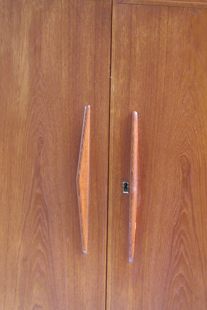Armoire vintage en bois des années 60 avec deux portes, deux tiroirs, poignées sculptées et pieds compas.